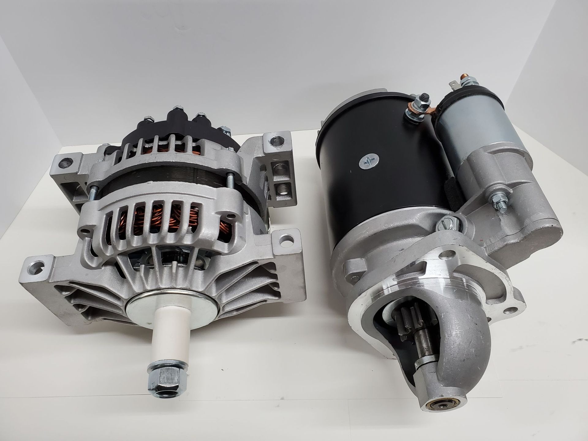 Two automotive starter motors on a light background, one silver and one black with silver accents.