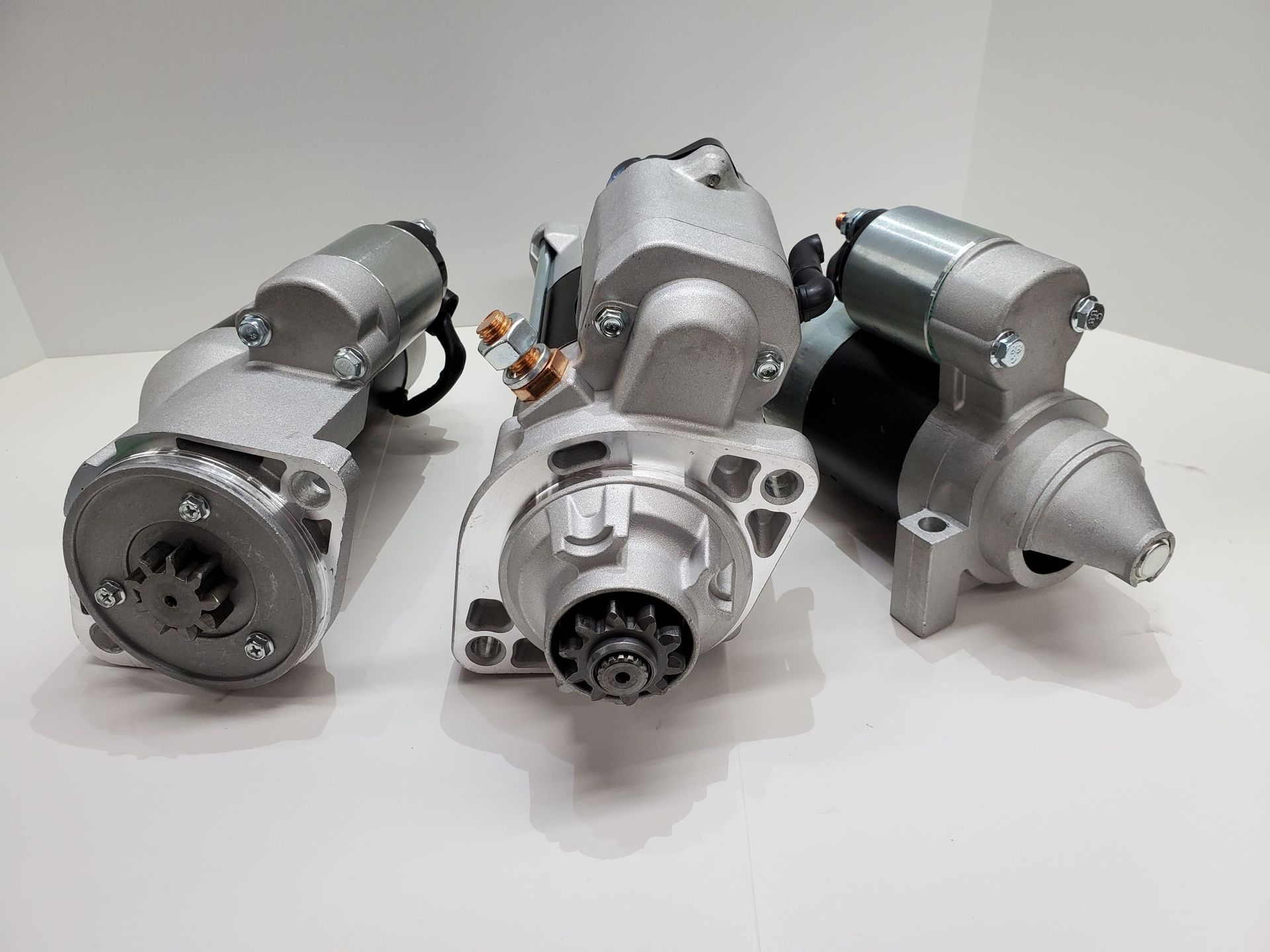Three metallic starter motors arranged on a white surface against a plain background
