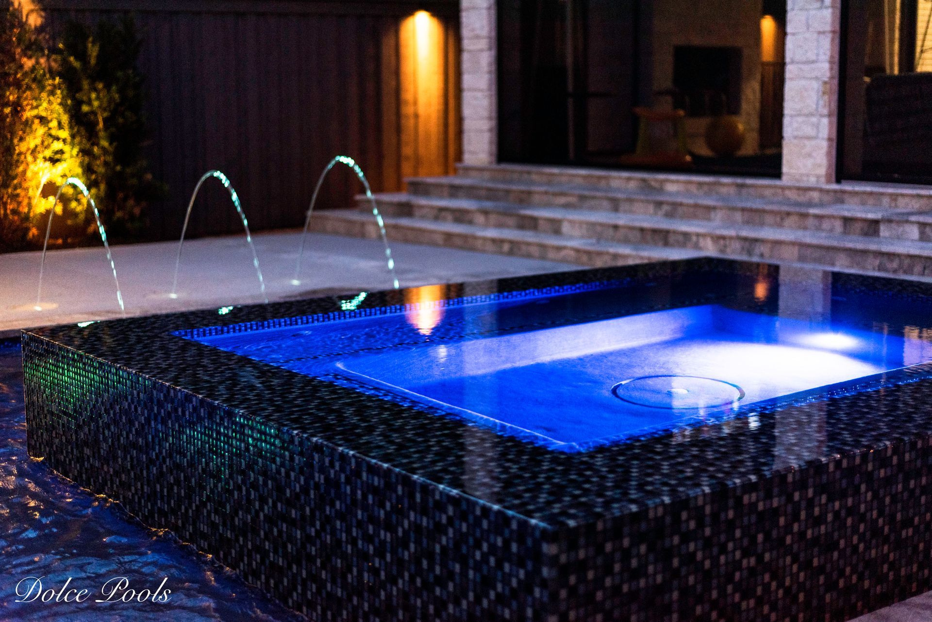 pool lit at night with blue lights and fountains