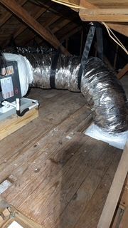 A duct is hanging from the ceiling of an attic.