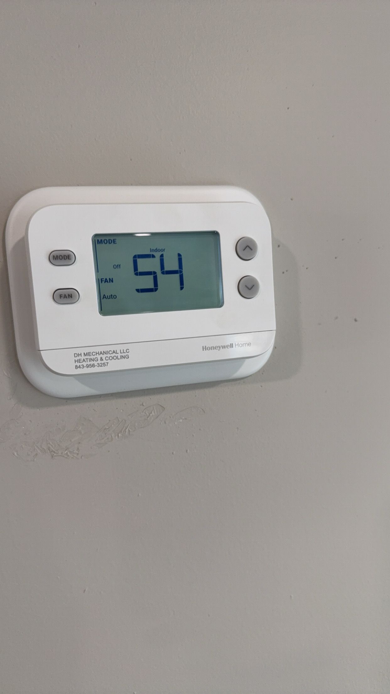A white digital thermostat is hanging on a wall.