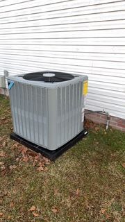 A large air conditioner is sitting in the grass next to a house.