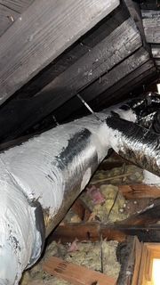 A pipe is hanging from the ceiling of an attic.