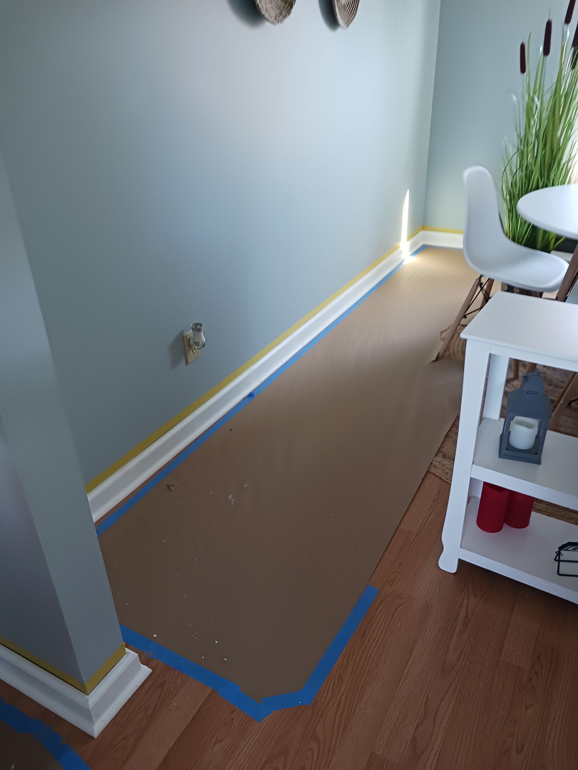 Room prepared for painting; walls blue, floor covered with cardboard, taped baseboards.