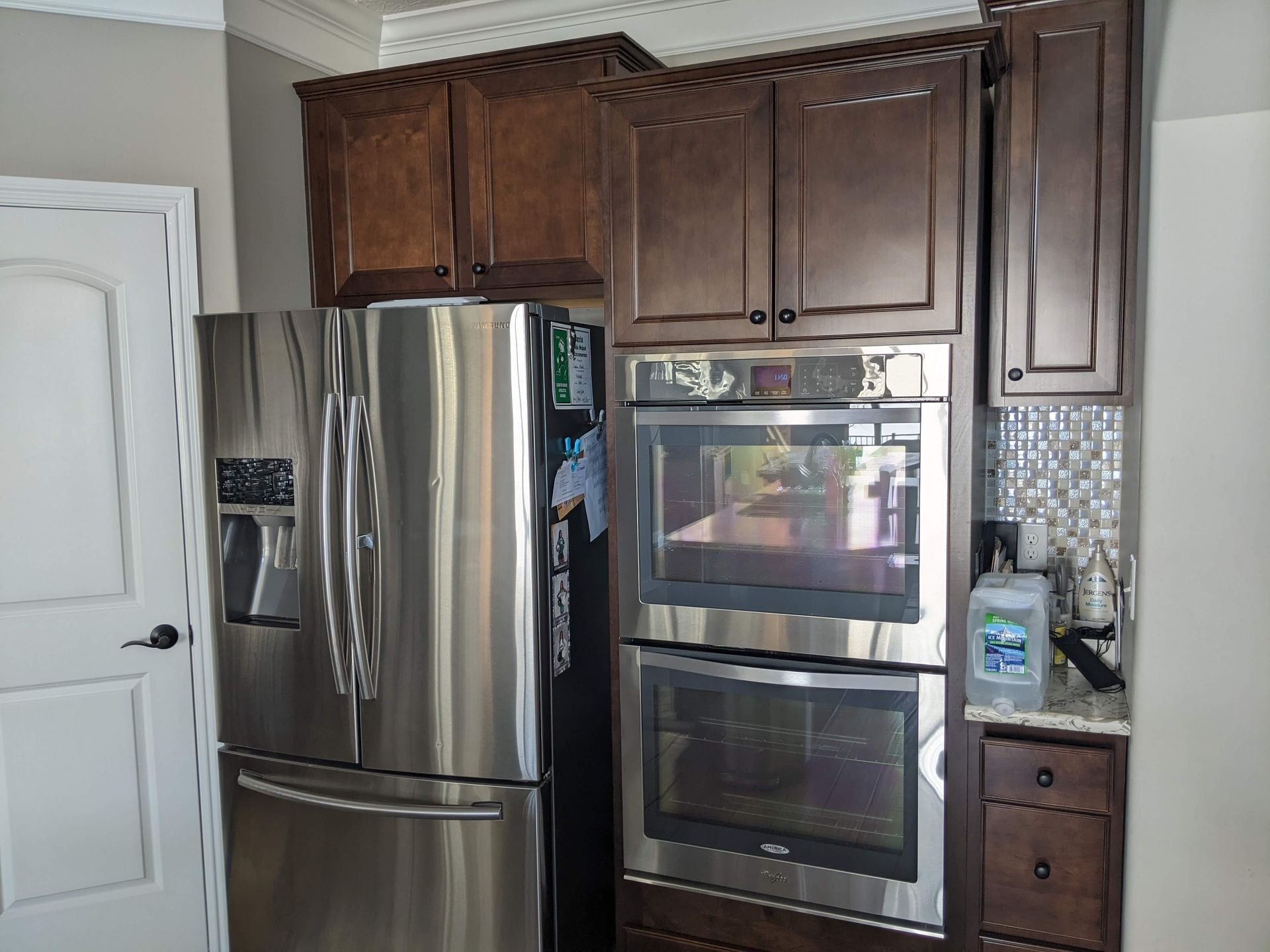Stainless steel refrigerator and double oven built into dark wood cabinets in a kitchen.