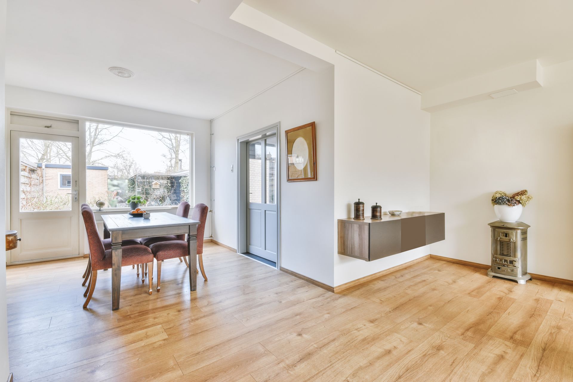 Dining room with table, chairs, large window, wood floor, and floating cabinet.