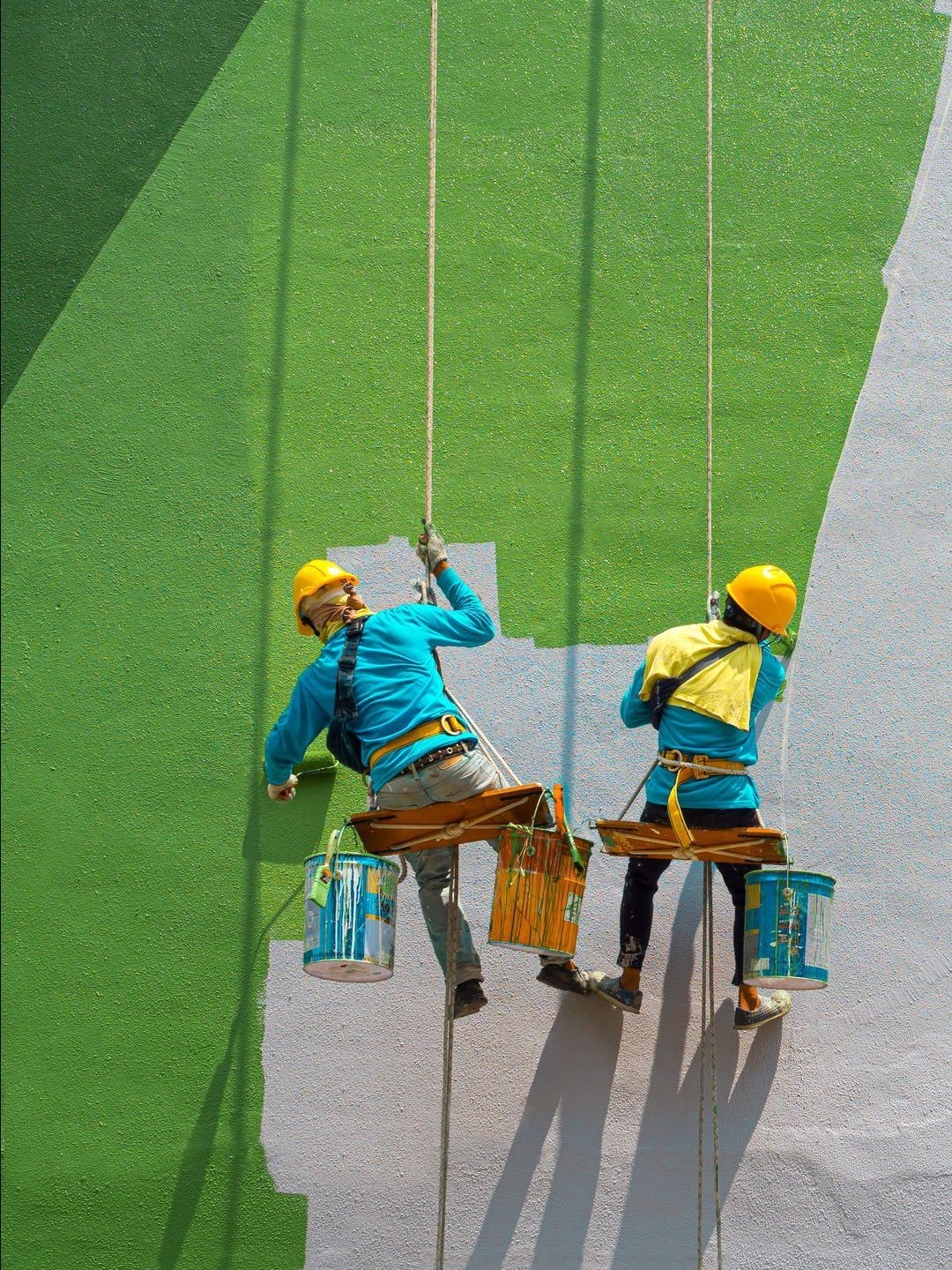 Two men are painting a wall on a rope.