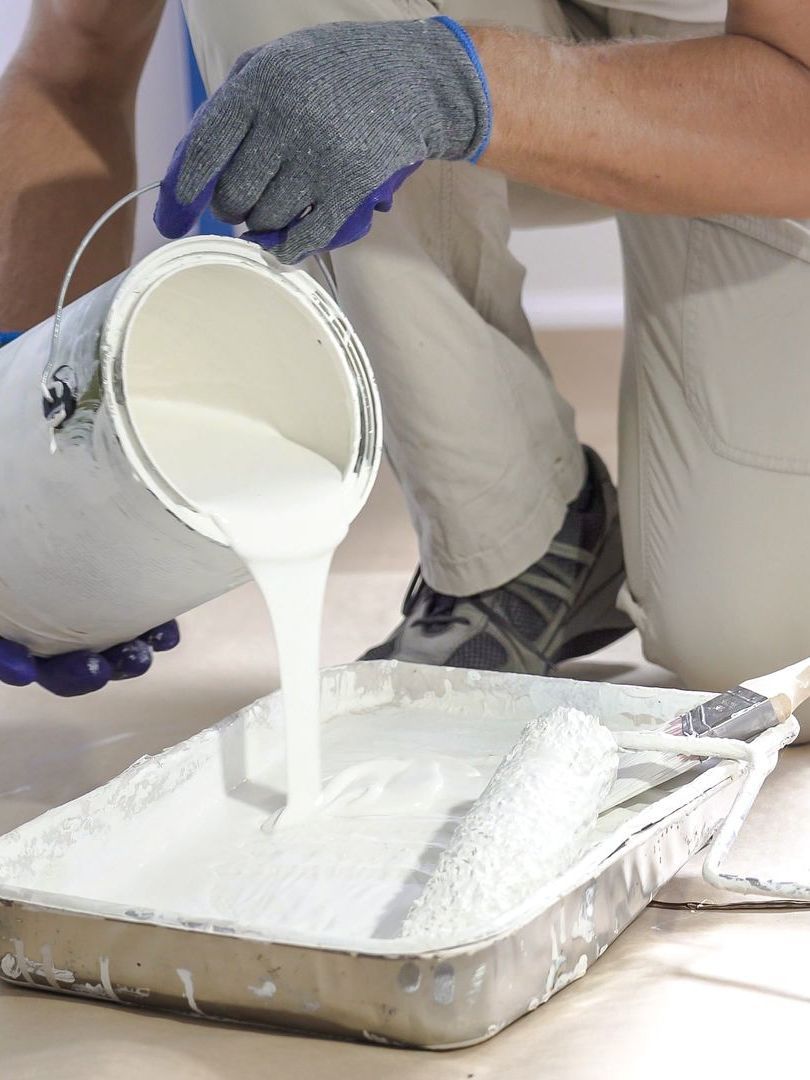 A person is pouring white paint into a tray.
