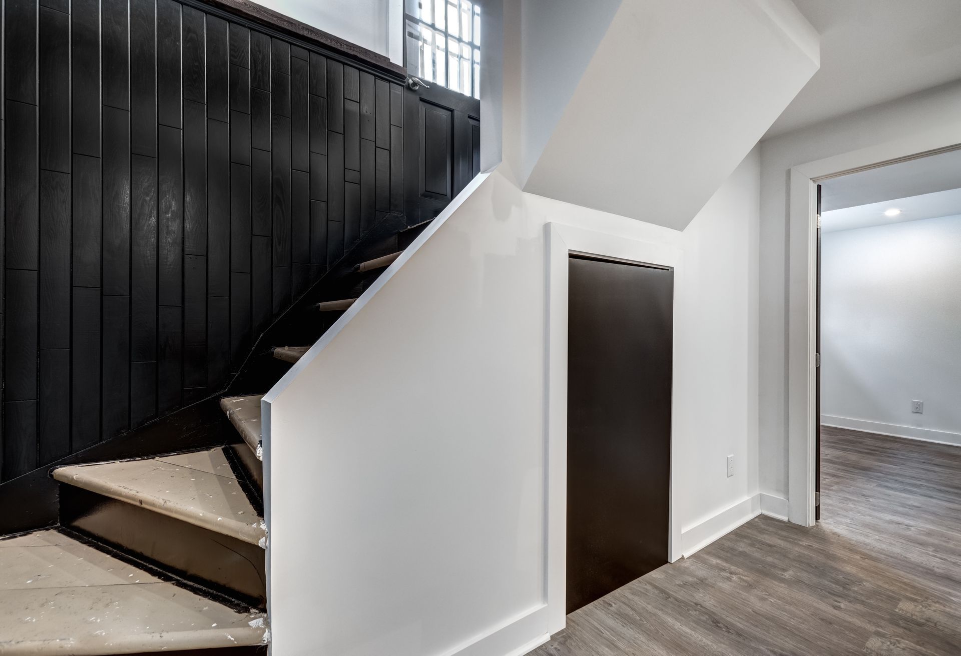 Staircase with black wall paneling, white walls, and a dark storage door. Light-colored flooring.