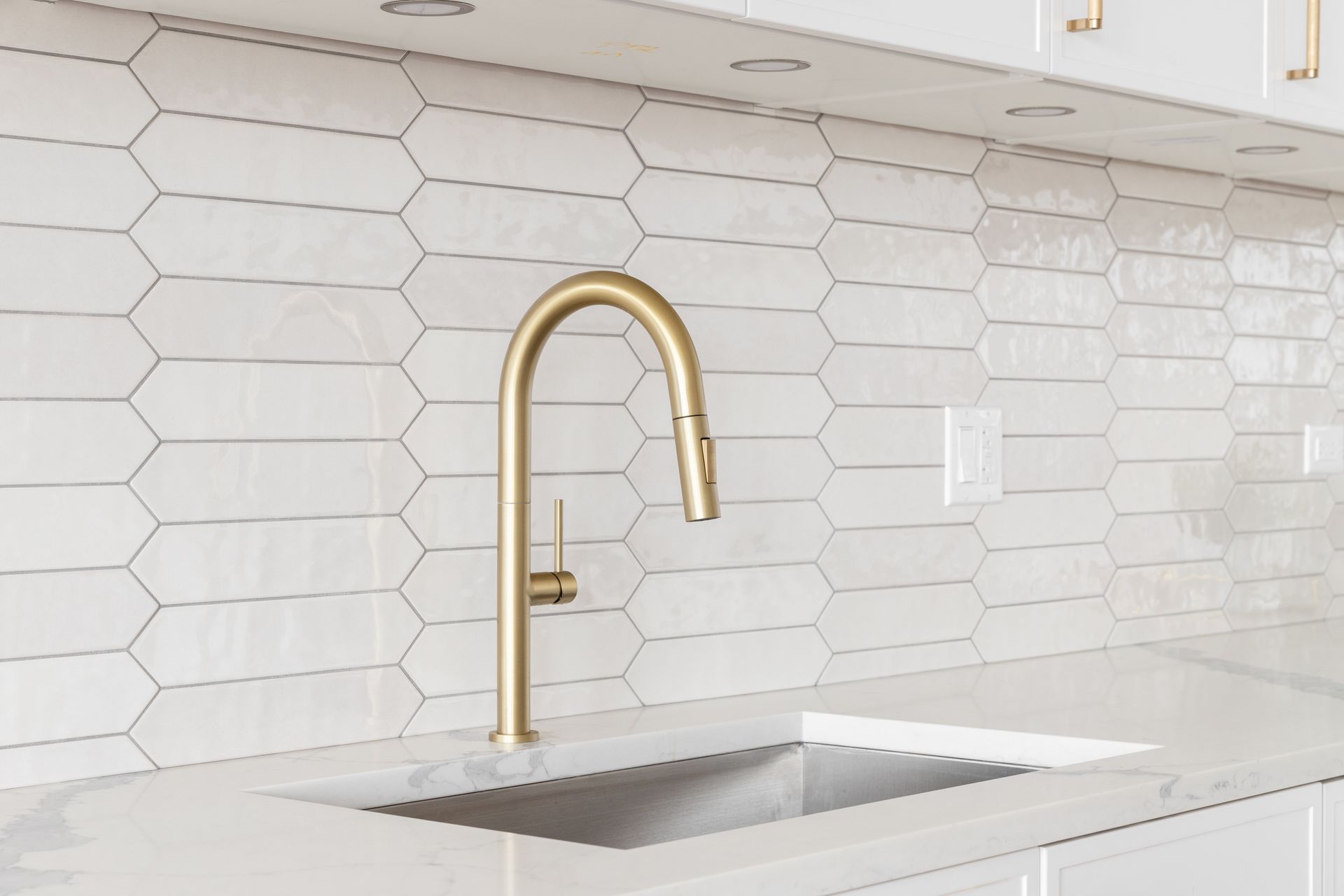 A kitchen sink with a brass faucet and white tiles on the wall.