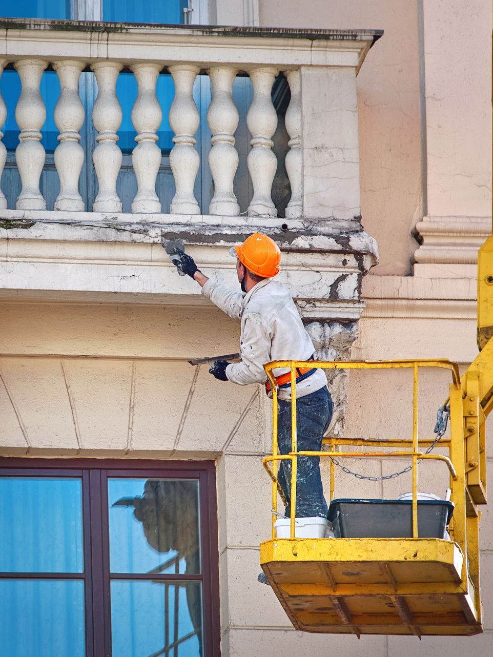 A man is painting a balcony on a building.
