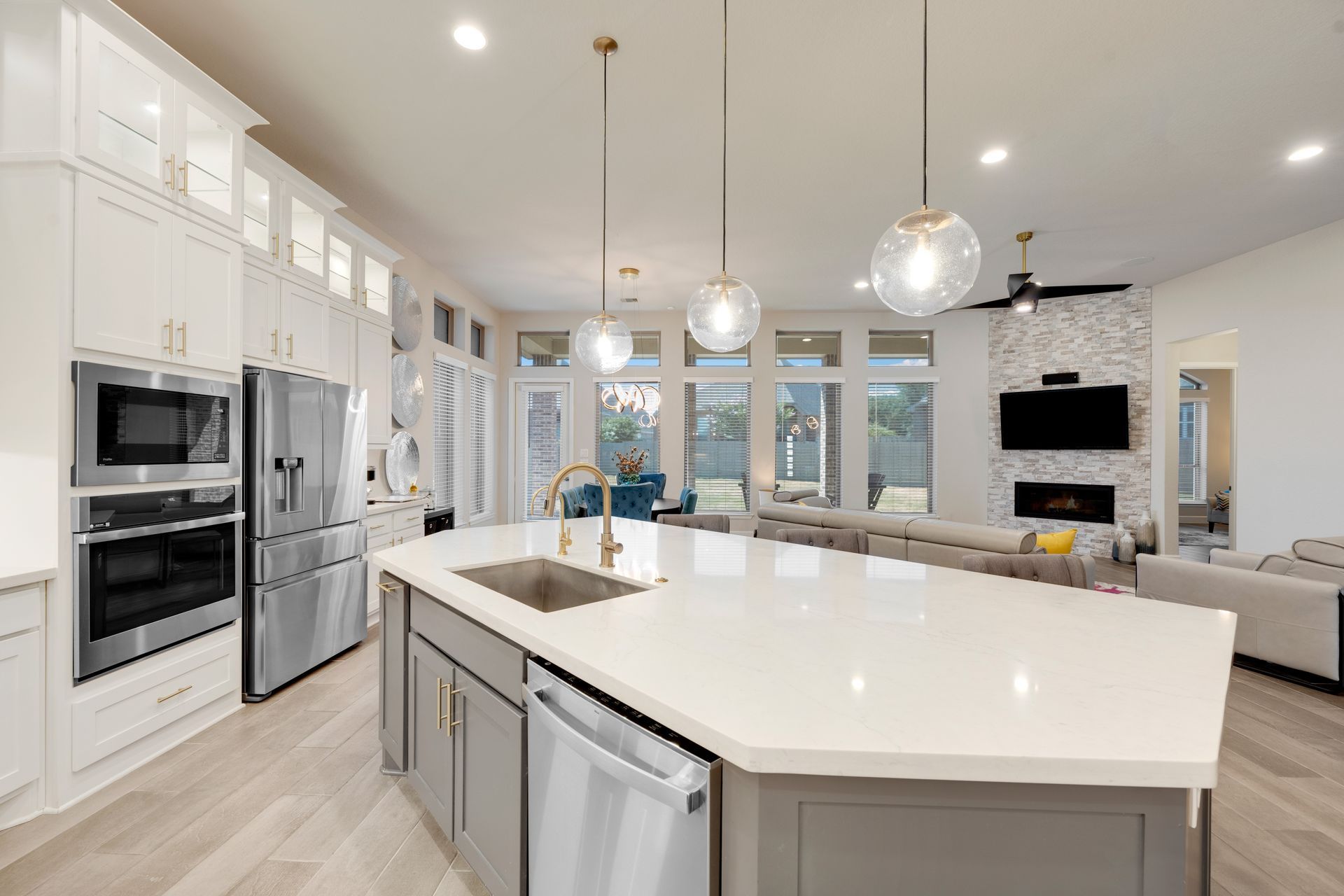 Modern kitchen with island, stainless steel appliances, white cabinets, and living area with fireplace.