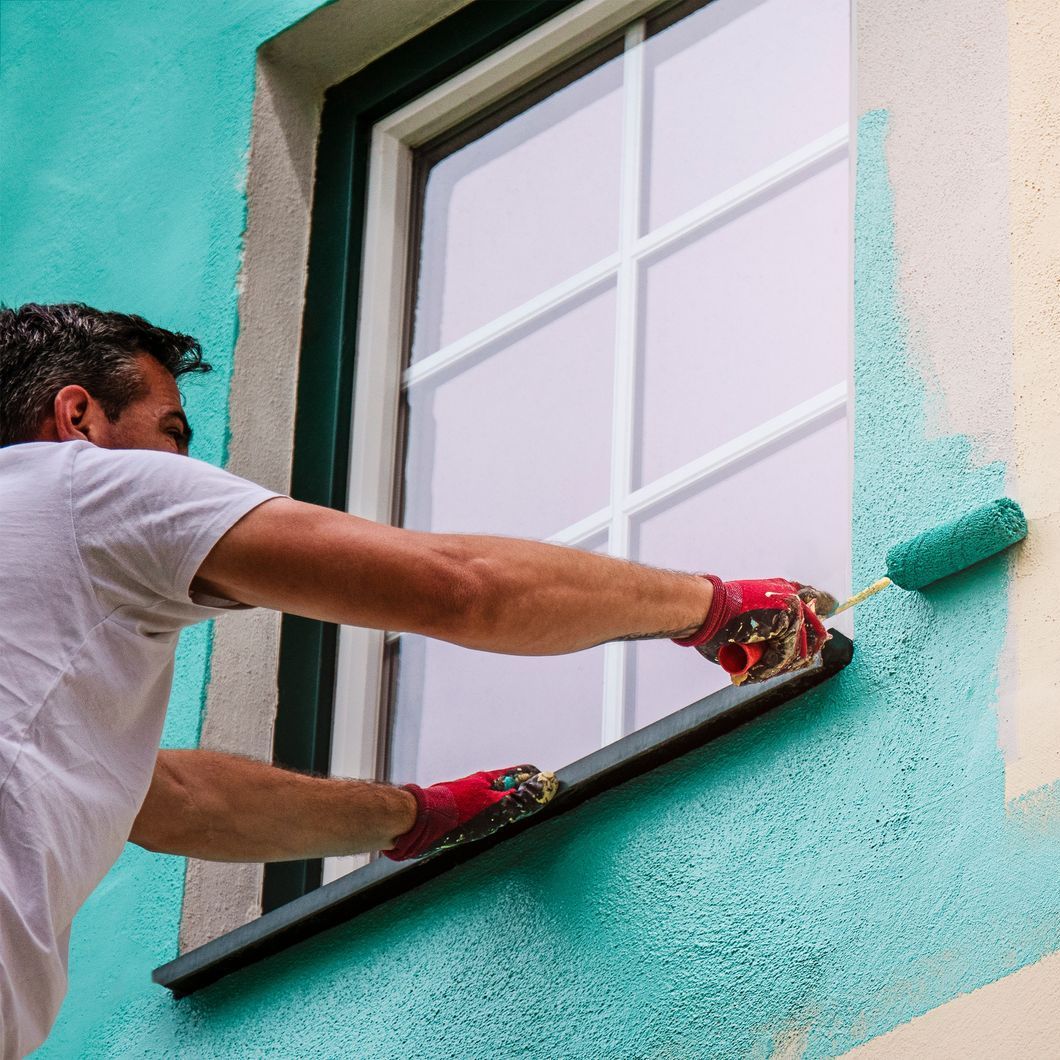A man is painting the side of a building with a roller.