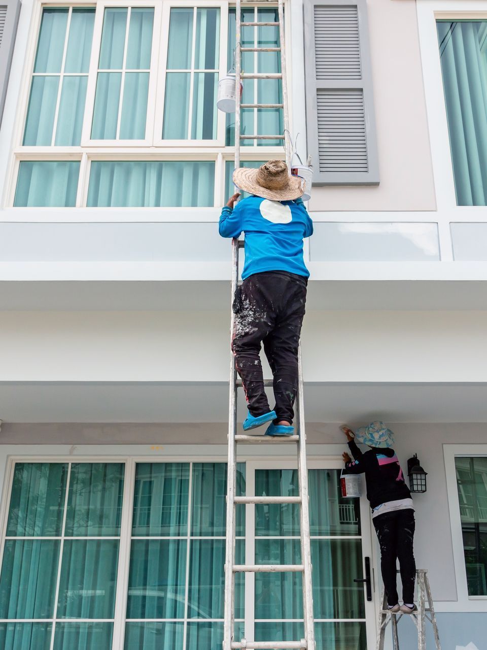 A man is standing on a ladder painting a house.