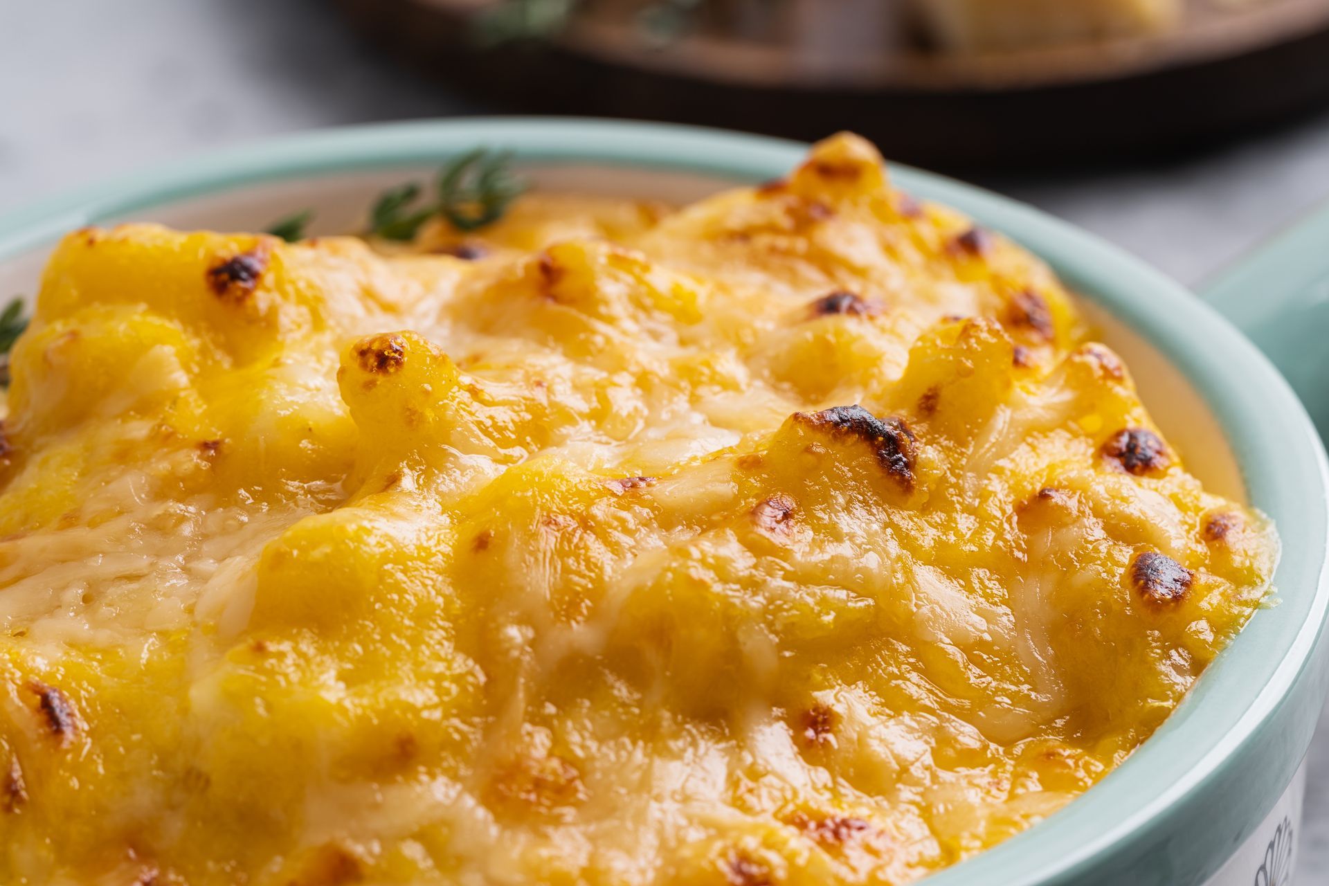 A close-up of a bubbling, cheesy macaroni dish served in a light blue ceramic bowl.