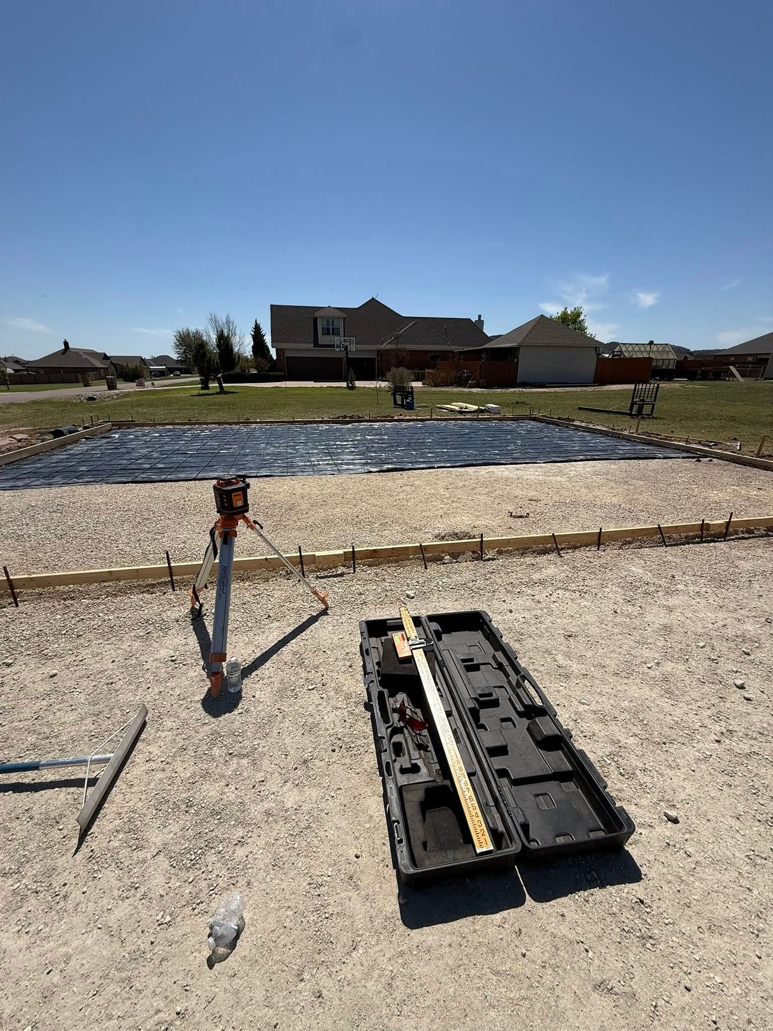 Backyard construction scene with gravel, a trench, tools, and a house in the background