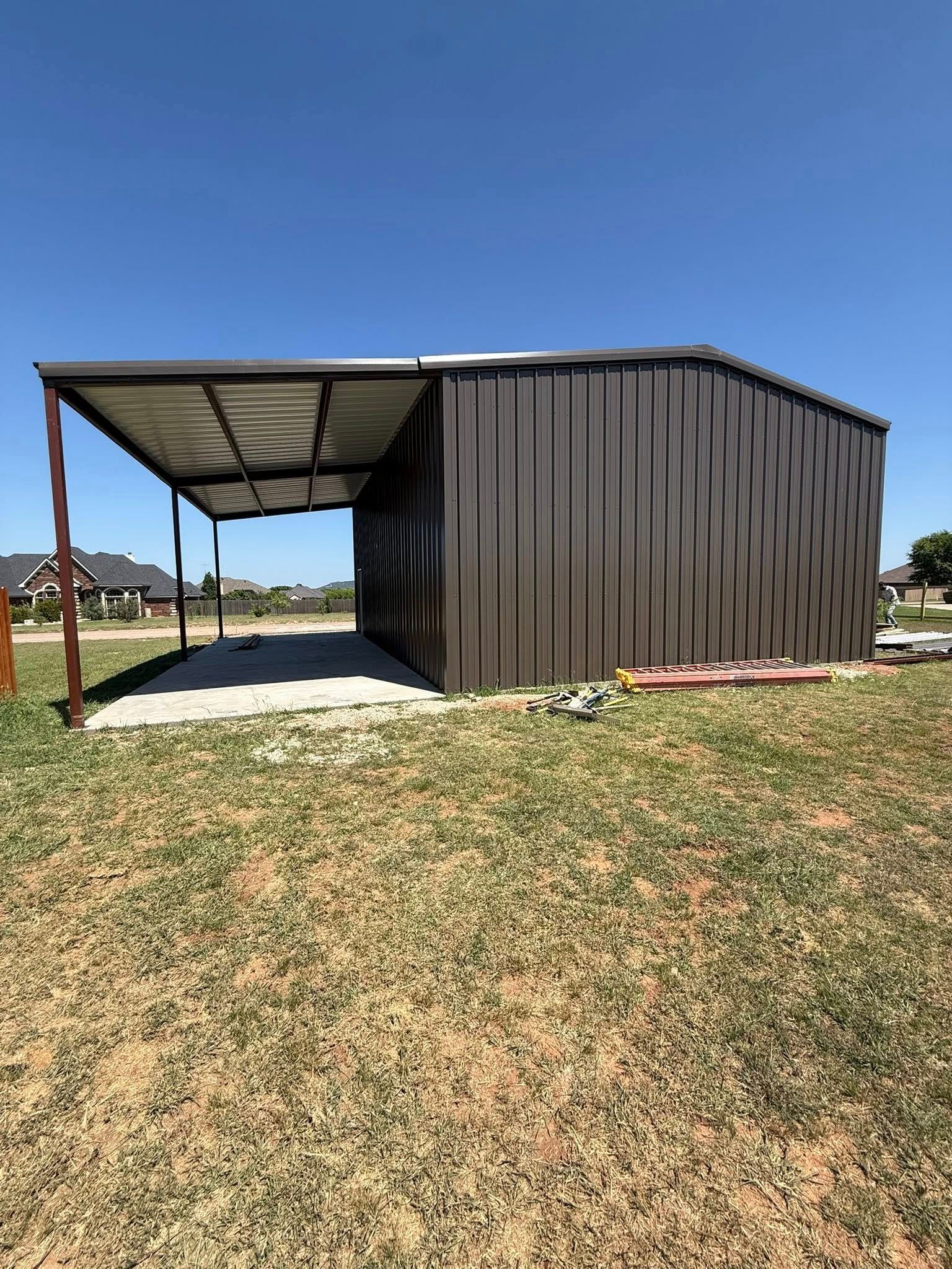 Metal shed with a corrugated roof beside a grassy field under a clear blue sky
