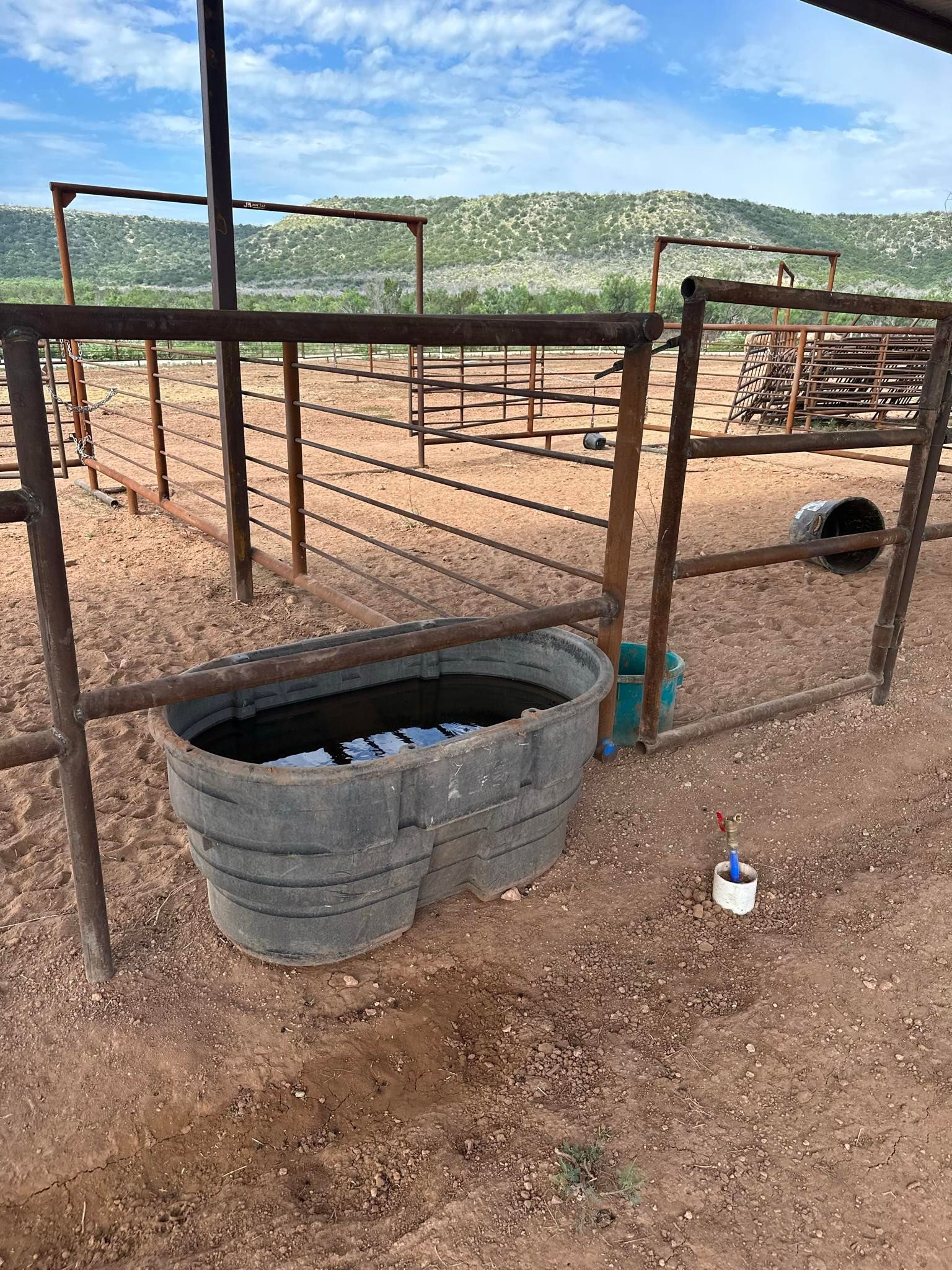 Rusty fenced animal pen with troughs and hills in the background