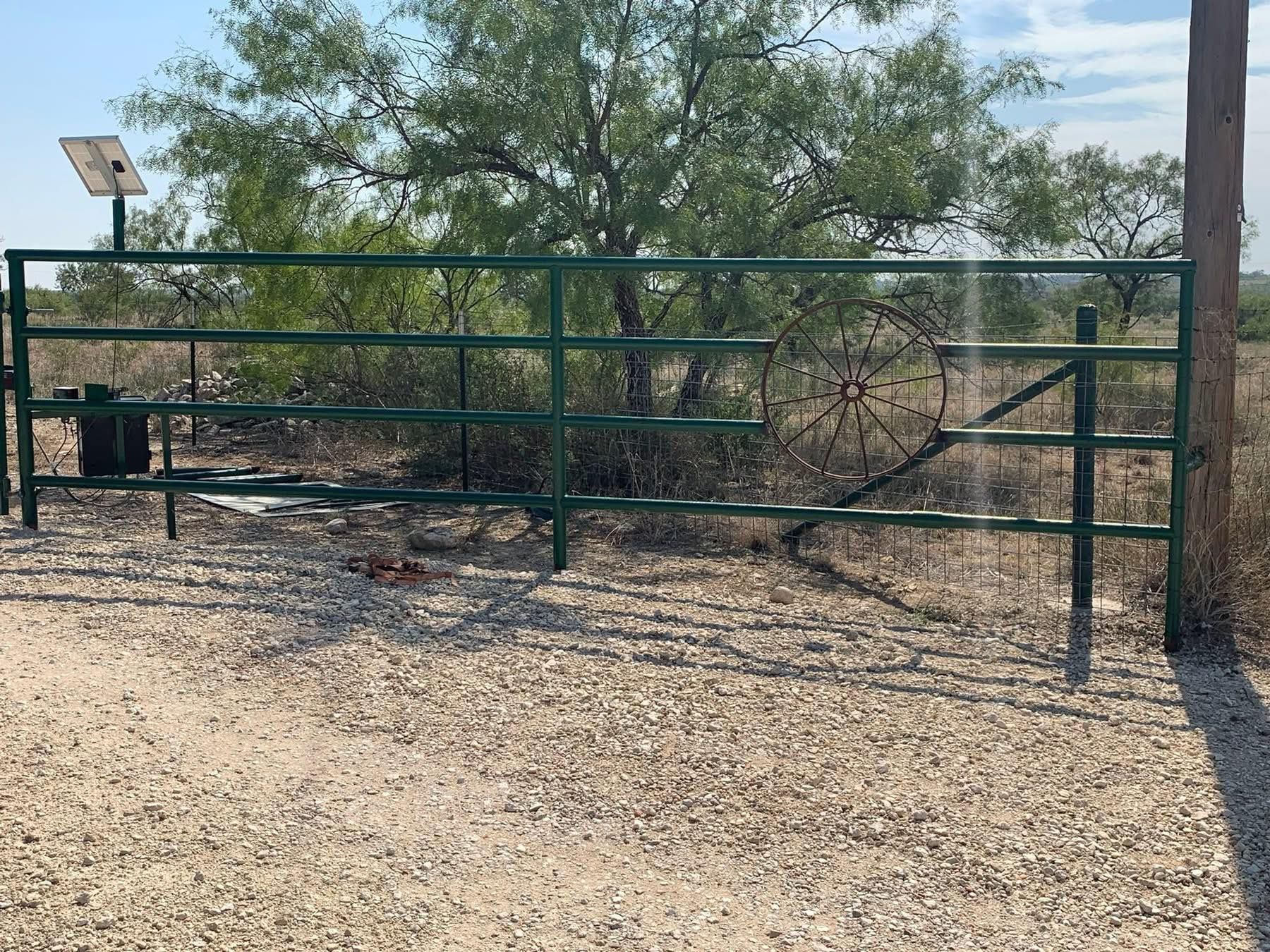 Green metal gate across a gravel driveway in a desert roadside setting