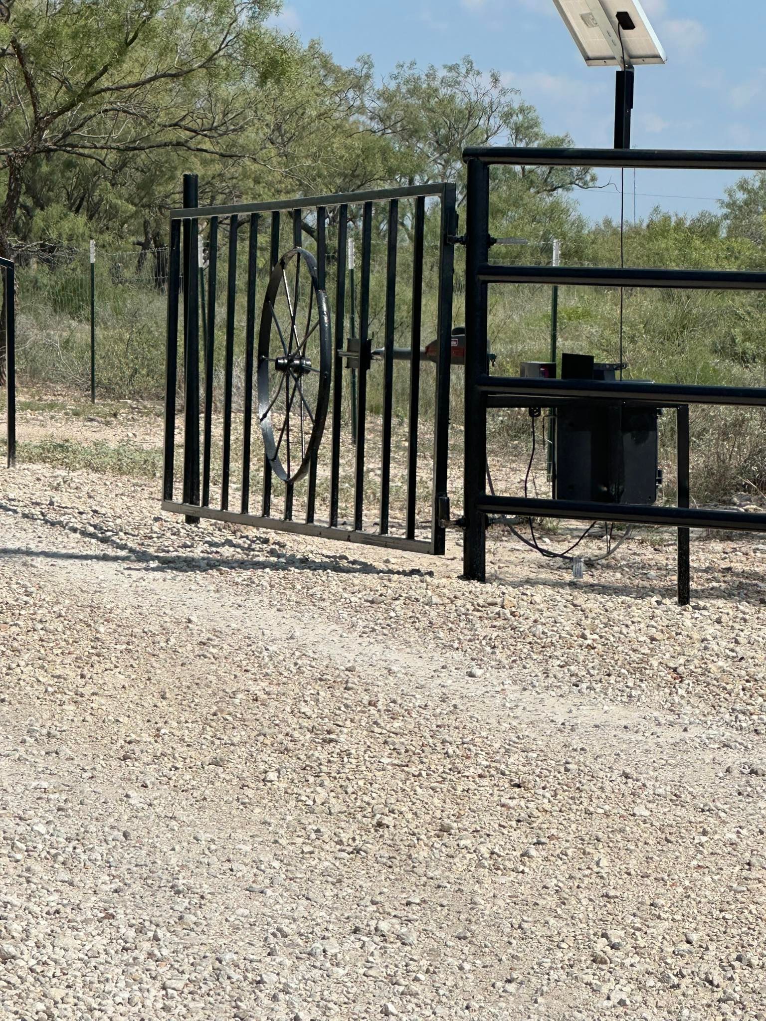 Black metal gate beside a fenced enclosure and solar light on a gravel path in a dry outdoor area