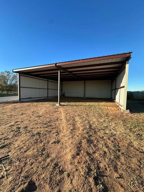 Open-sided metal shed with a rusted roof on a gravel lot under a blue sky