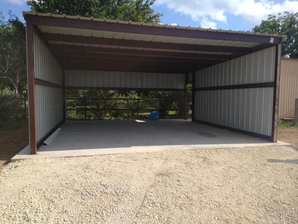 Open metal-sided carport with a concrete floor and trees visible behind it