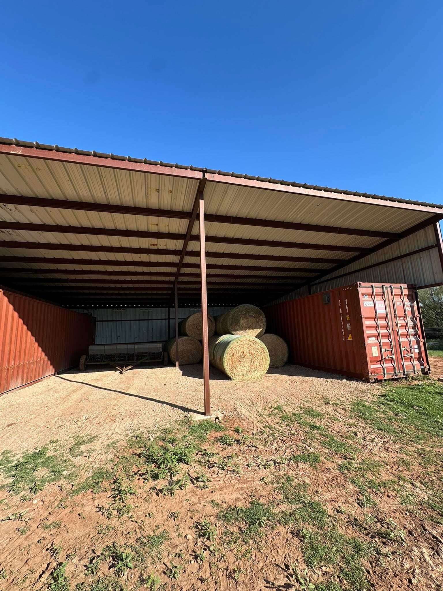 Open-sided shed with hay bales and red shipping containers under a blue sky