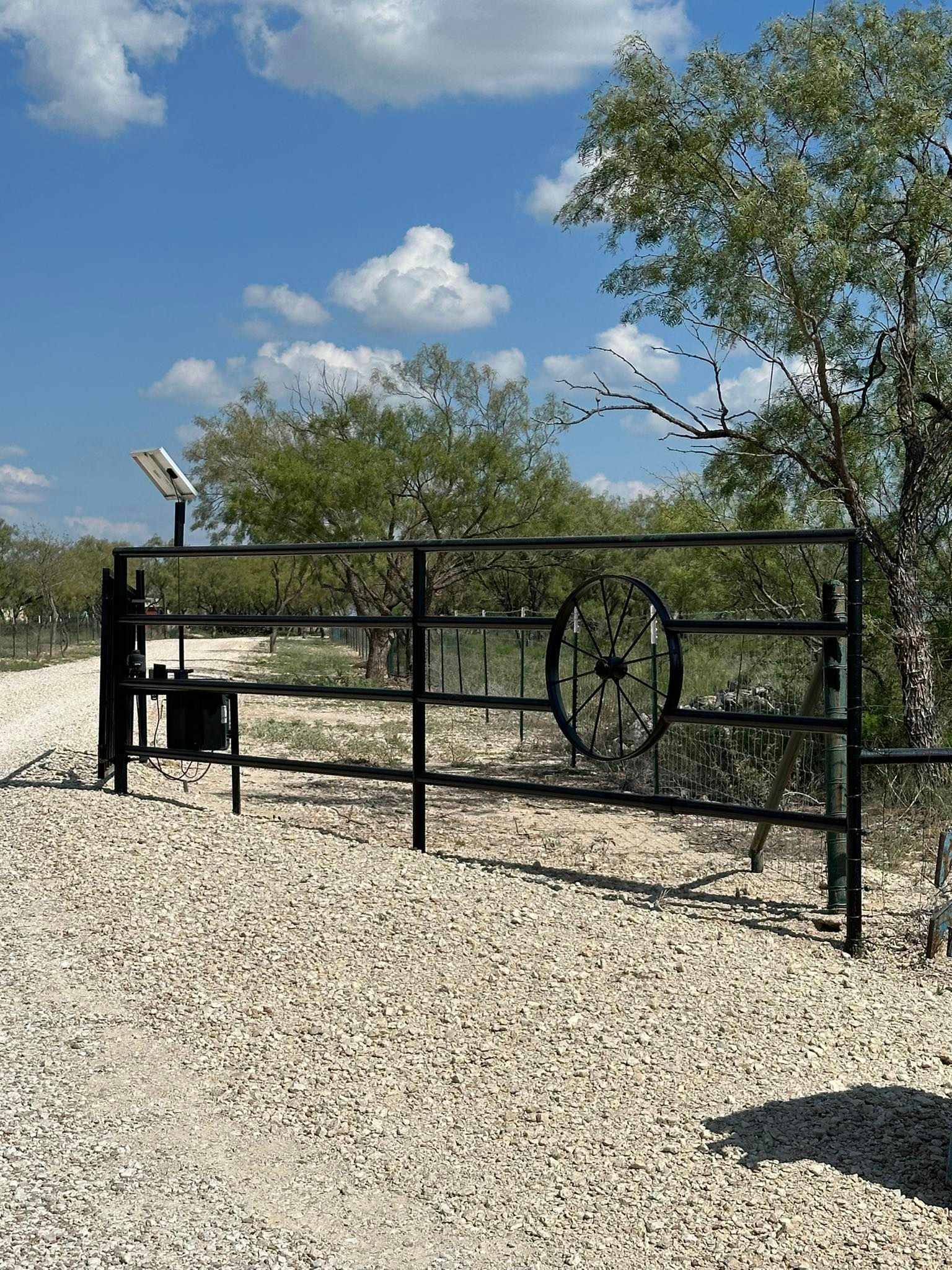 Black metal gate on a gravel driveway with trees and blue sky in the background