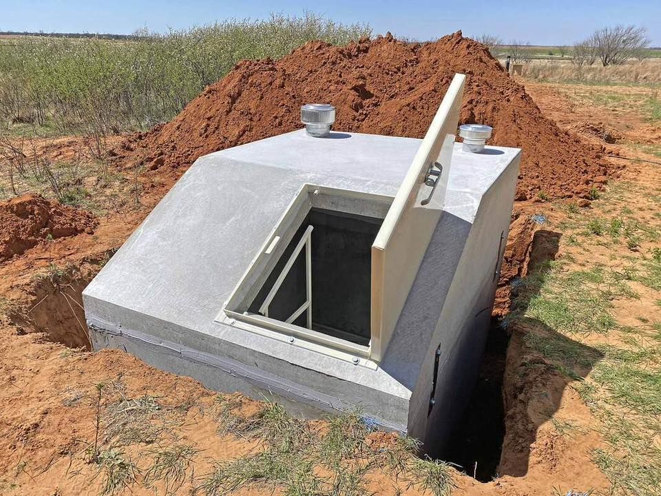 Concrete underground hatch with open metal door beside a dirt mound in a rural field