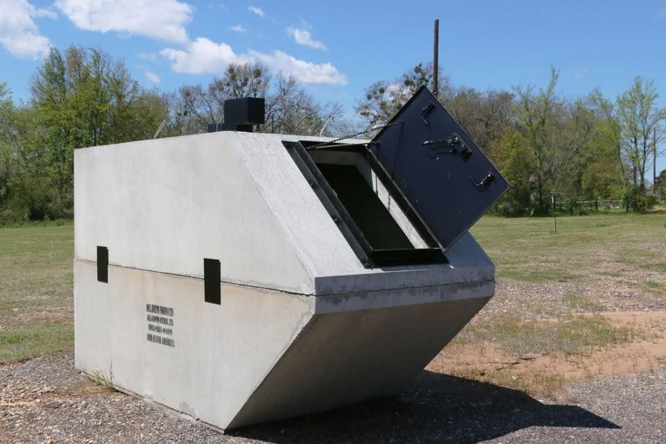 Large white outdoor metal bunker or shelter with an open black hatch in a grassy field