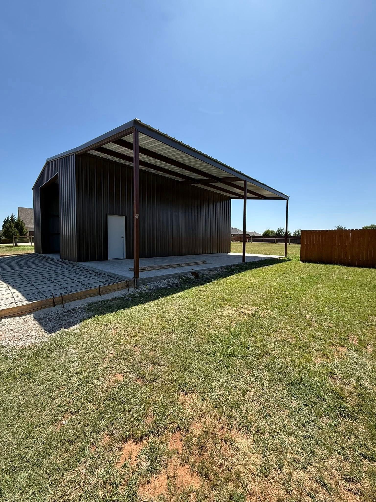 Small metal shed with a covered porch on a grassy lot under a clear blue sky