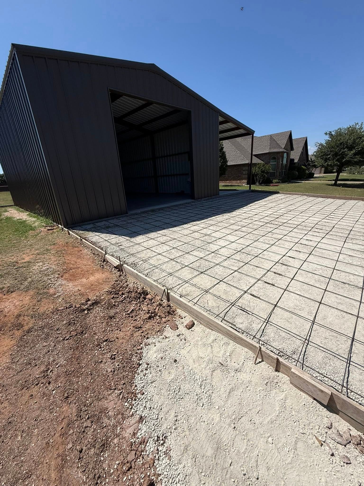Driveway leading to a dark metal carport beside a house on a sunny day