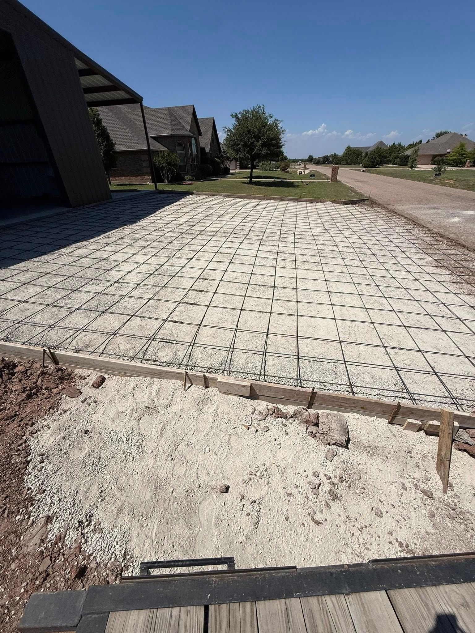Broken sidewalk beside houses and a dirt road under a bright blue sky.
