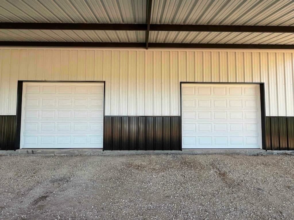 Two white garage doors on a metal building with a gravel foreground
