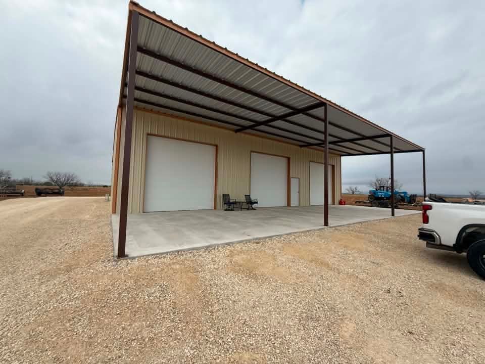 Gravel lot with a metal carport attached to a warehouse-style building and a white pickup truck nearby
