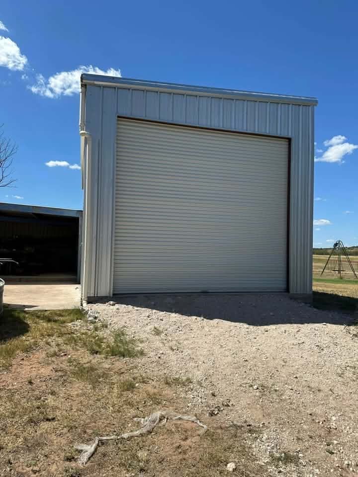 Small metal storage building with a large closed roll-up door under a blue sky.