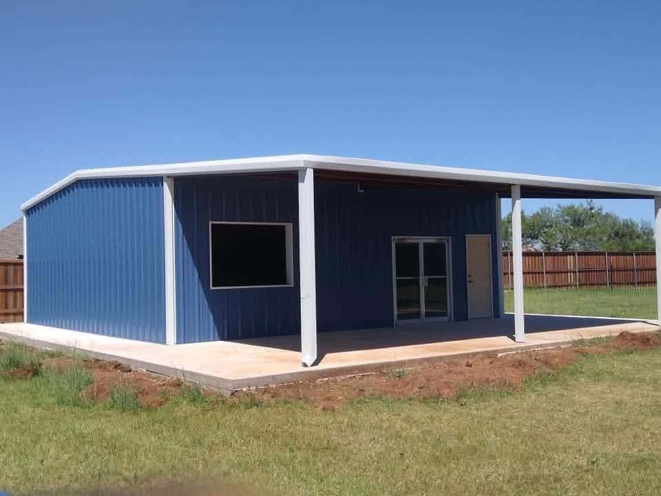 Blue metal shed with white trim and a covered porch in a grassy yard