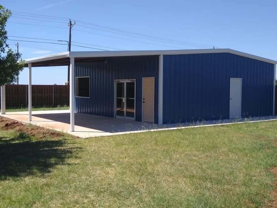 Blue metal building with white trim and covered porch on a grassy lot