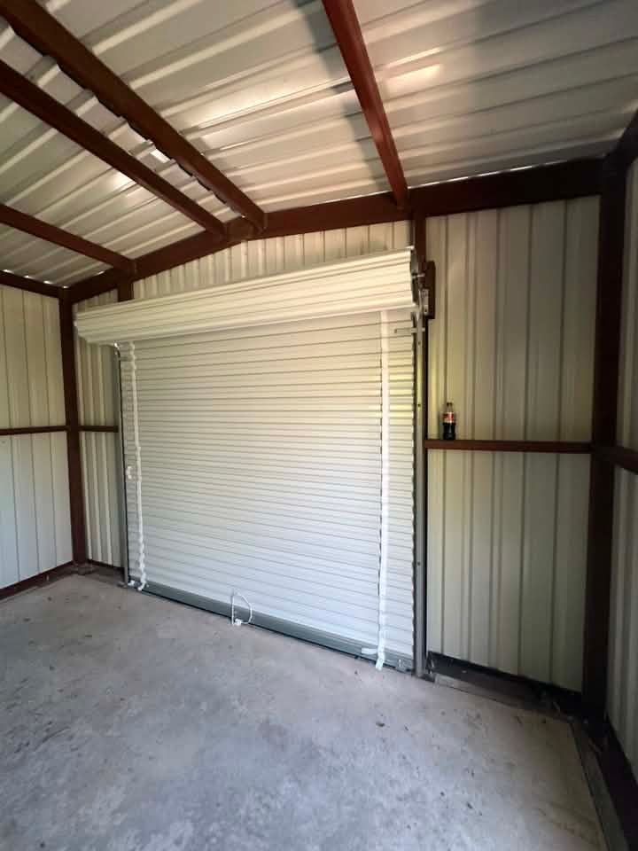 Interior of a small metal shed with a white roll-up door and concrete floor.
