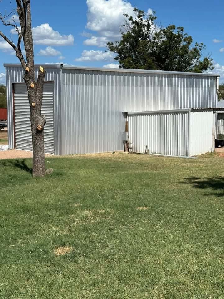 Silver metal shed and small white outbuilding on a grassy yard under a blue sky.