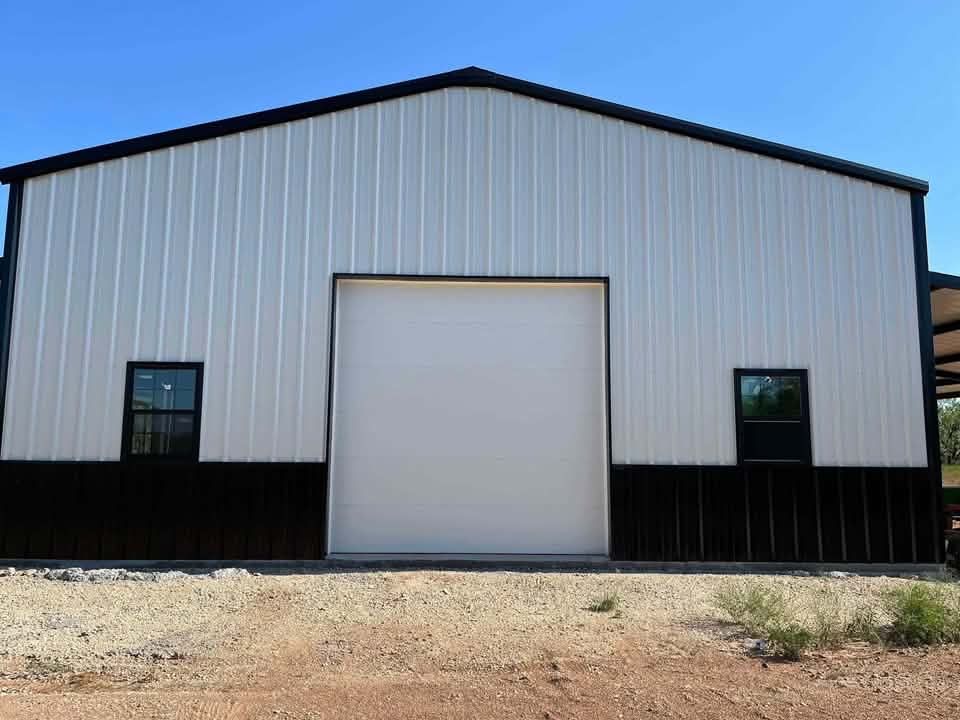 White metal warehouse with black trim and a large central garage door on a gravel lot.