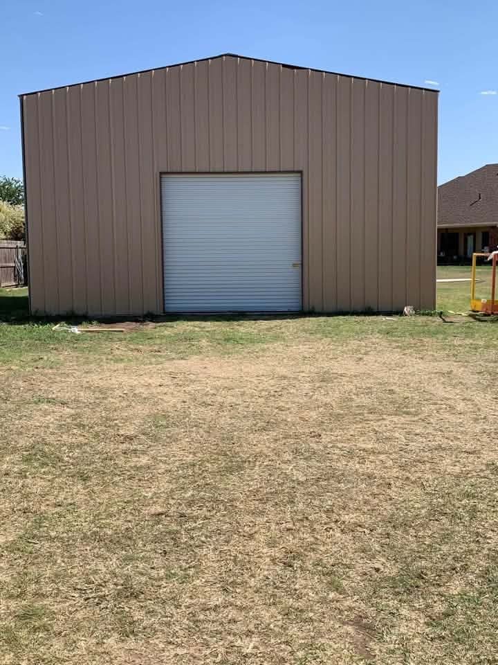 Brown metal storage shed with a white roll-up door on a dry grassy lot