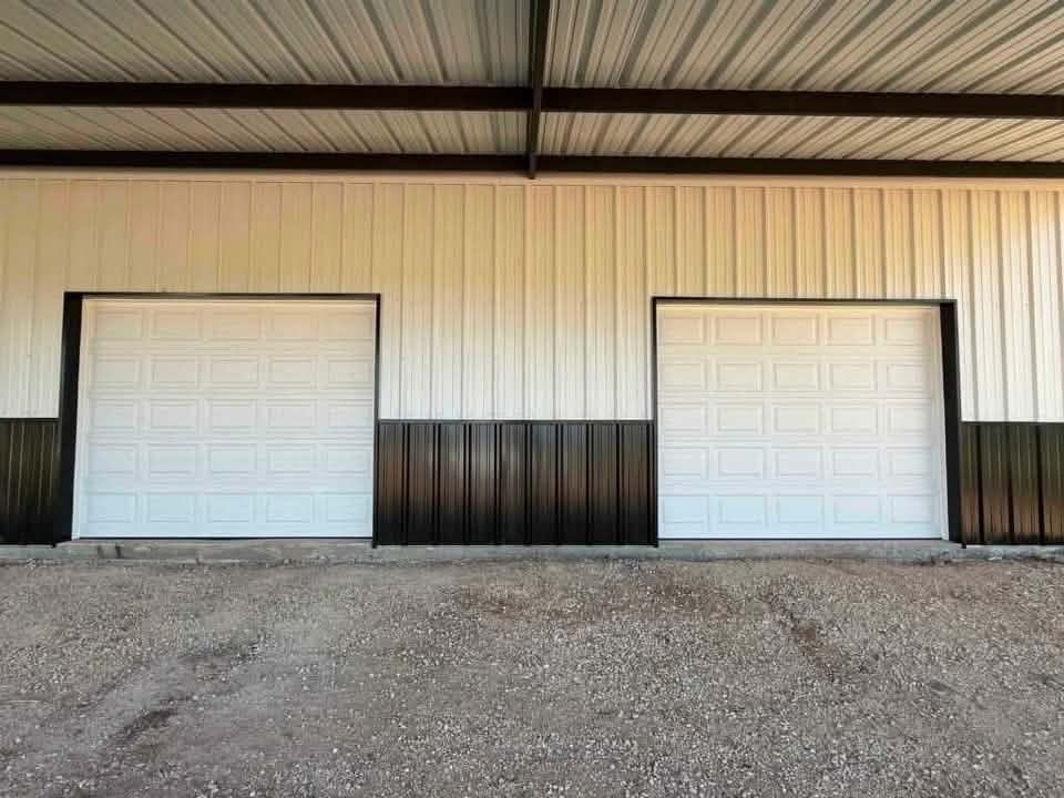 Two white garage doors on a beige metal building with black trim and gravel foreground