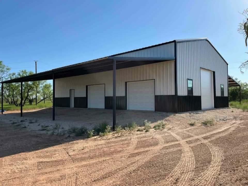Large metal shed with a covered front porch on a dirt lot under a clear sky