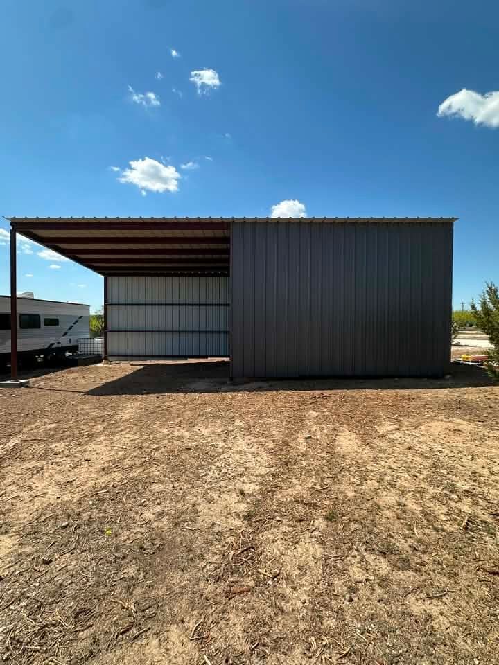 Metal storage shed with a covered side bay in a dry, open lot under a blue sky