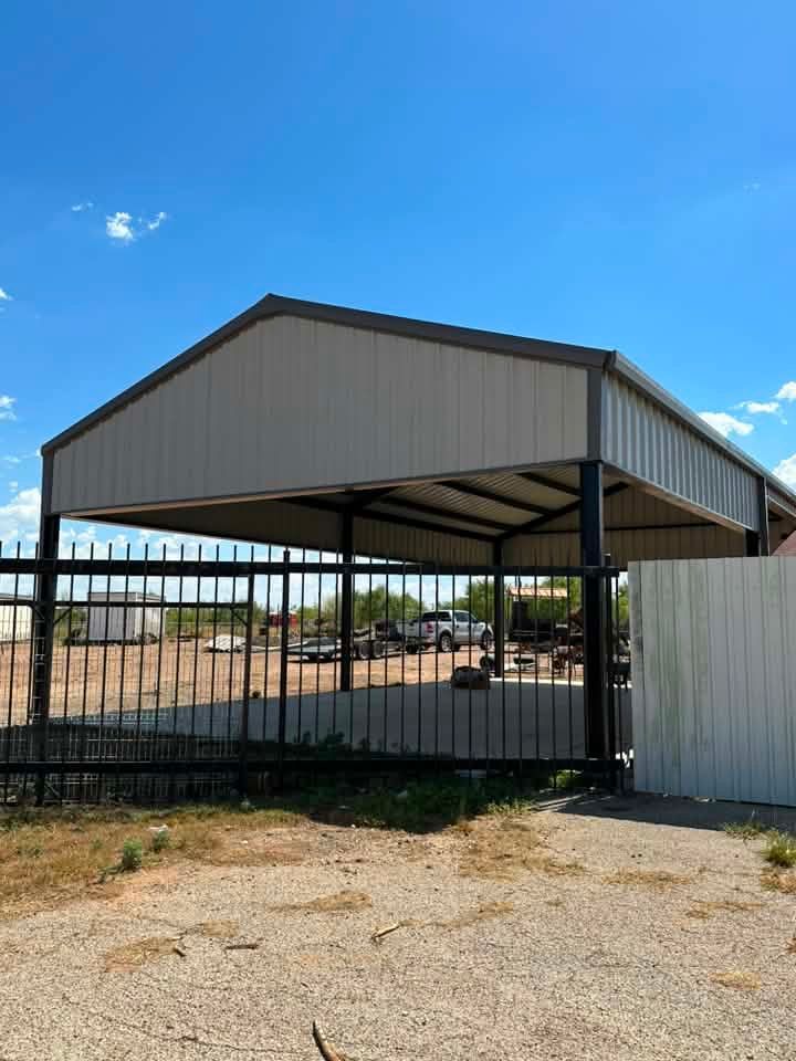 Black metal carport with white roof beside a fence under a clear blue sky