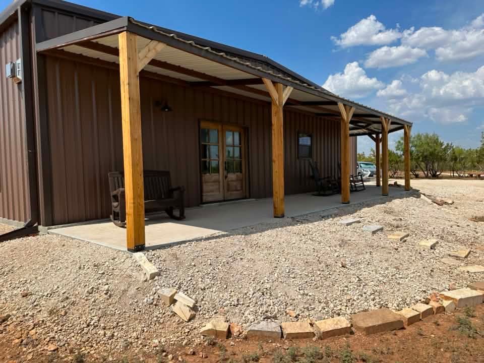 Brown cabin with a covered porch and wooden posts in a rocky, open lot under a blue sky