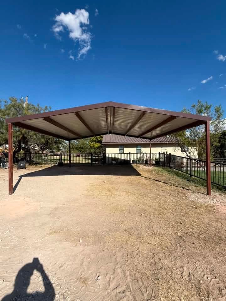 Open-sided metal carport with a gravel floor under a blue sky, viewed from the entrance