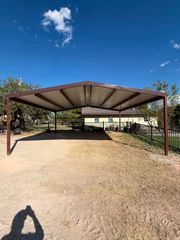 Open-sided metal pavilion with a dirt floor under a blue sky on a sunny day