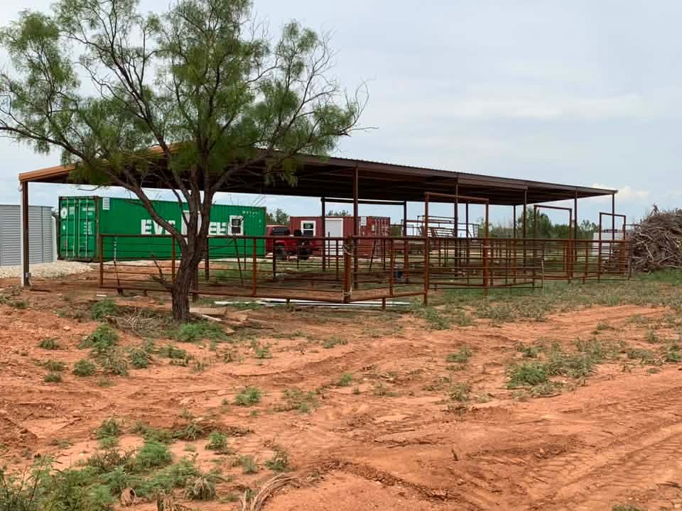 Open-sided shelter with red fencing beside a green shipping container on a dry, rural hillside